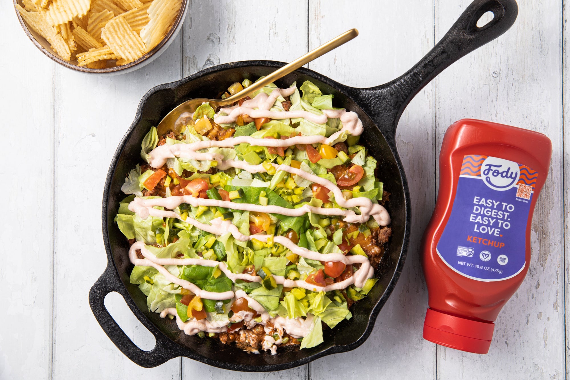 An image of Fody's skillet cheeseburger dip on a table in a cast iron pan next to a bottle of Fody's ketchup.