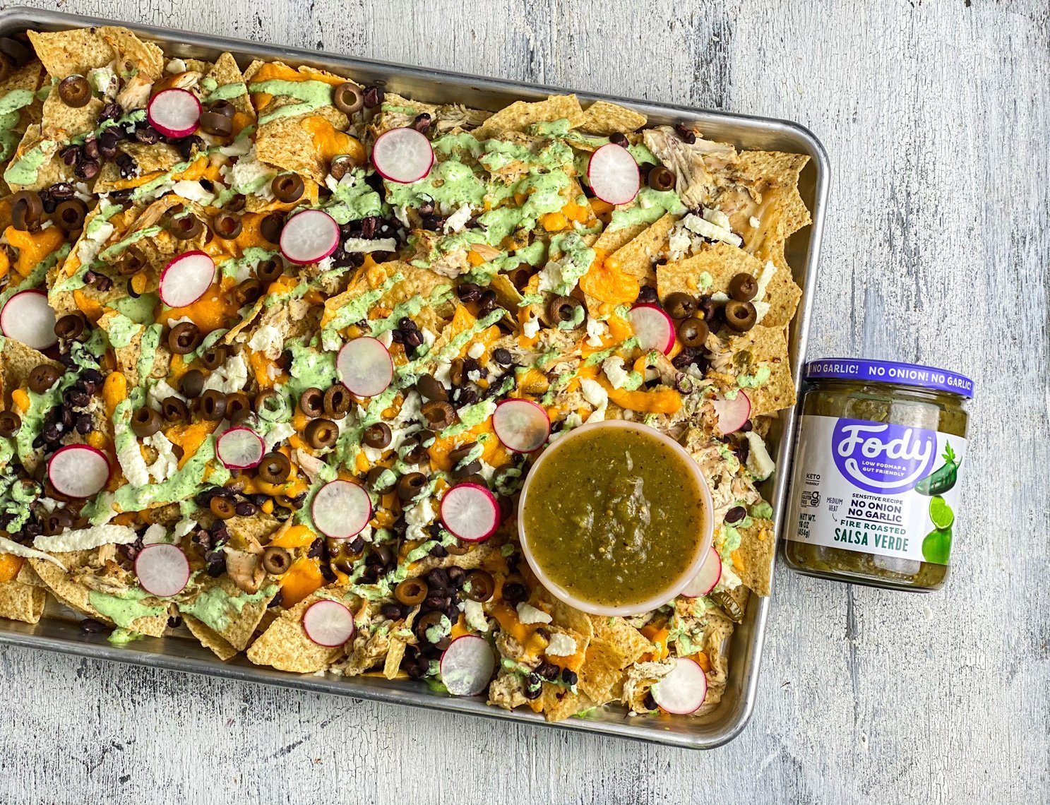 loaded salsa verde chicken nachos with jalapeño crema next to Fody's Low FODMAP salsa verde
