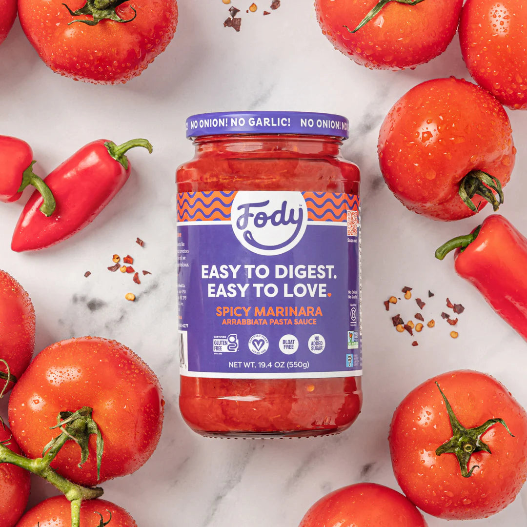 An image of ripe red tomatoes and red chilis laid out around a jar of Fody’s Spicy Marinara Arrabiata pasta sauce.
