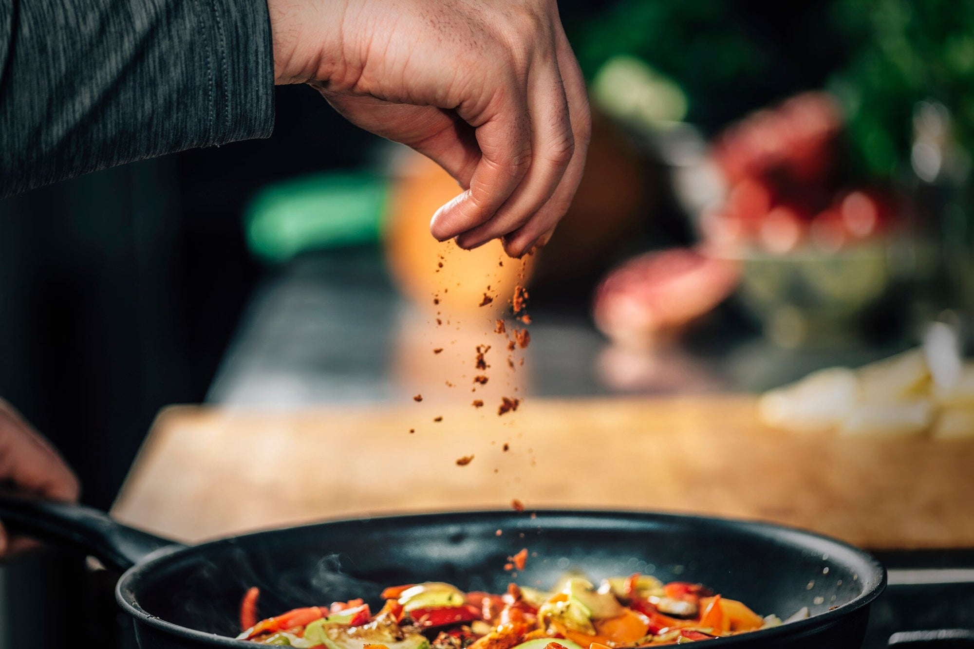 Image of a hand sprinkling spices all over a pan of spicy food.