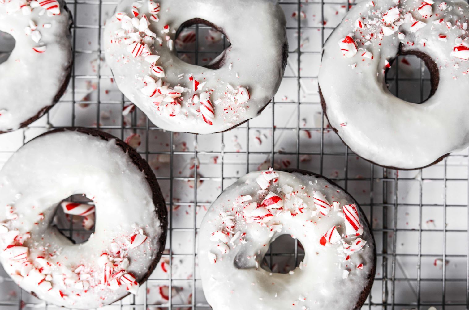 A cooling rack covered with a holiday treat: Fody's Chocolate Peppermint Glazed Donuts. These gluten-free donuts are chocolate colored, with a white glaze and a sprinkling of crushed candy cane.