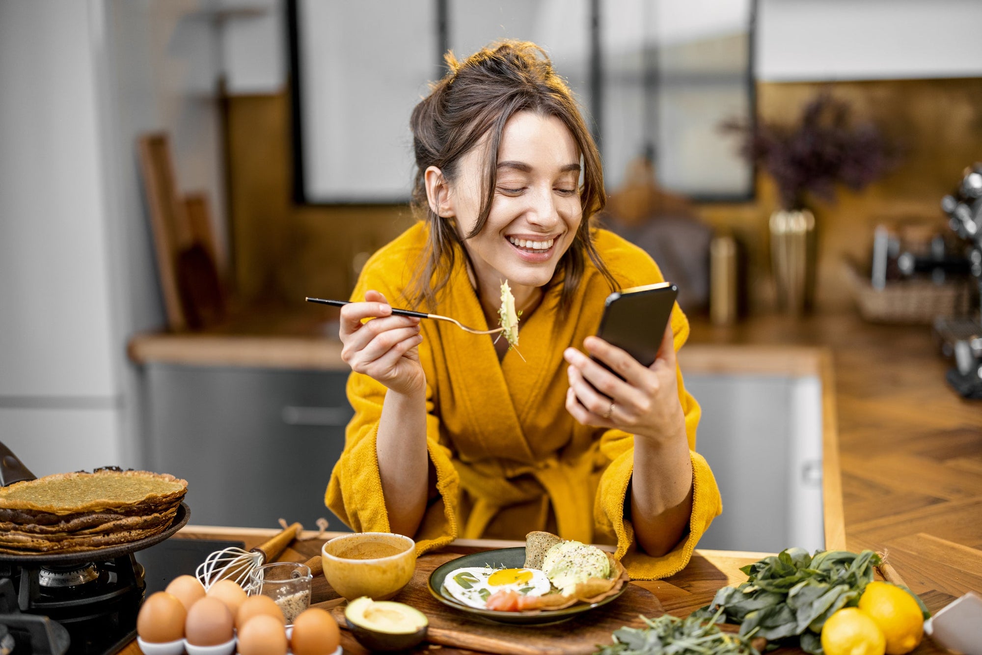 A young woman checking her phone while enjoying a healthy no-bloat breakfast of eggs.