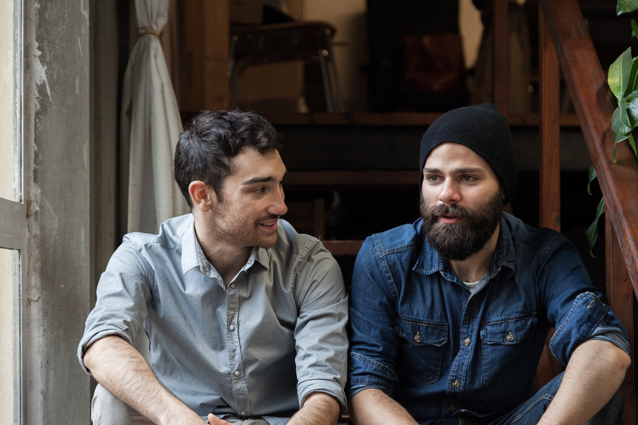 Knowing how to have difficult conversations about IBS can go a long way towards having productive discussions! Image: Two young men sit on the steps of a building, talking comfortably.