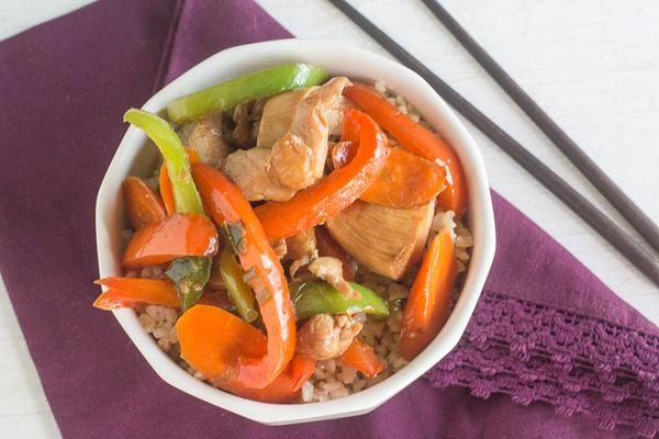 Low FODMAP chicken stir fry with red and green bell peppers and carrots, served over rice in a white bowl with chopsticks on the side