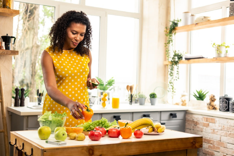 Gut health and mental health are more closely linked than you might think! Image: A woman plans a meal while looking thoughtfully at an assortment of brightly coloured vegetables on the counter of her sunny kitchen.