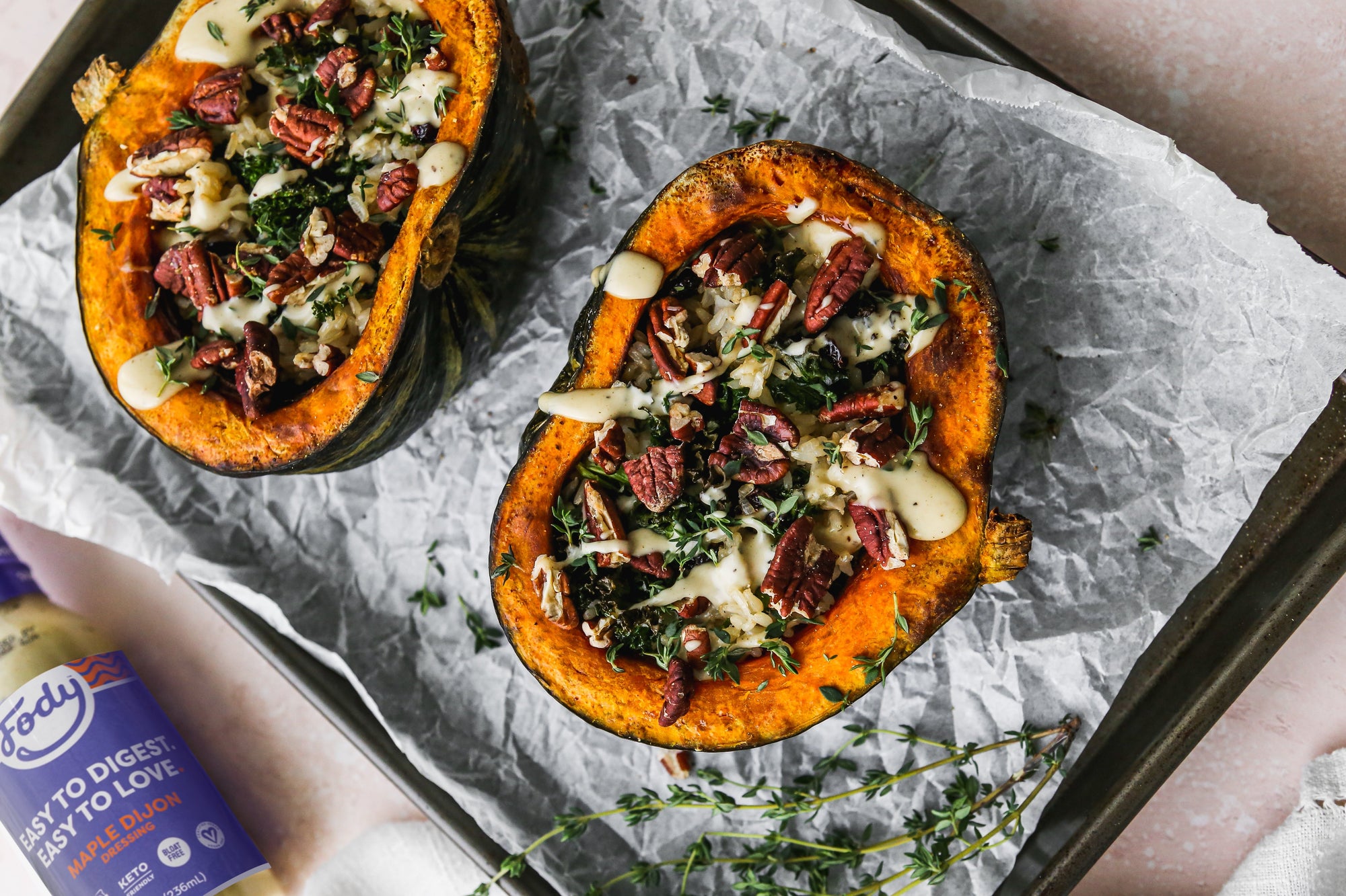 Image of a low-FODMAP stuffed kabocha squash side dish: two squash halves lie on a baking sheet, stuffed with vegetables and drizzled with Fody's maple dijon.