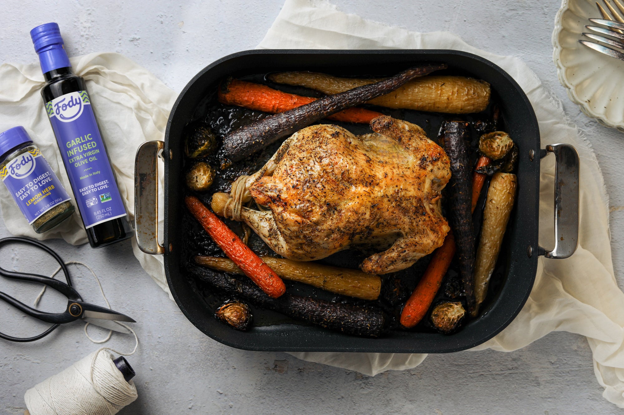 A Thanksgiving Roast Chicken in a Pan with parsnips, carrots and Brussels sprouts, beside a bottle of Fody-brand olive oil.