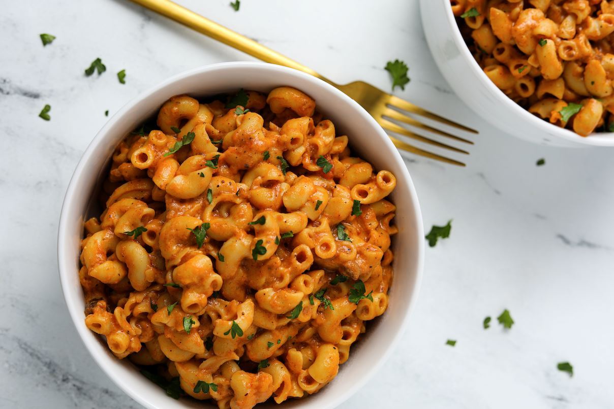 An image of a white bowl of vegan bolognese pasta on a white background beside a gold fork