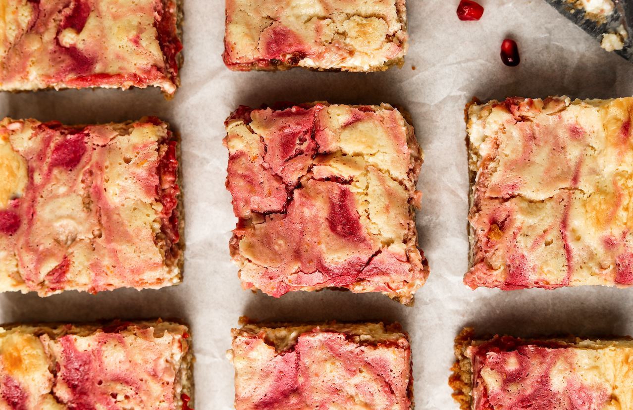 An image of low-FODMAP holiday desserts: squares of Fody's Pomegranate + Raspberry Swirl Cheesecake Bars neatly arranged over a light background.