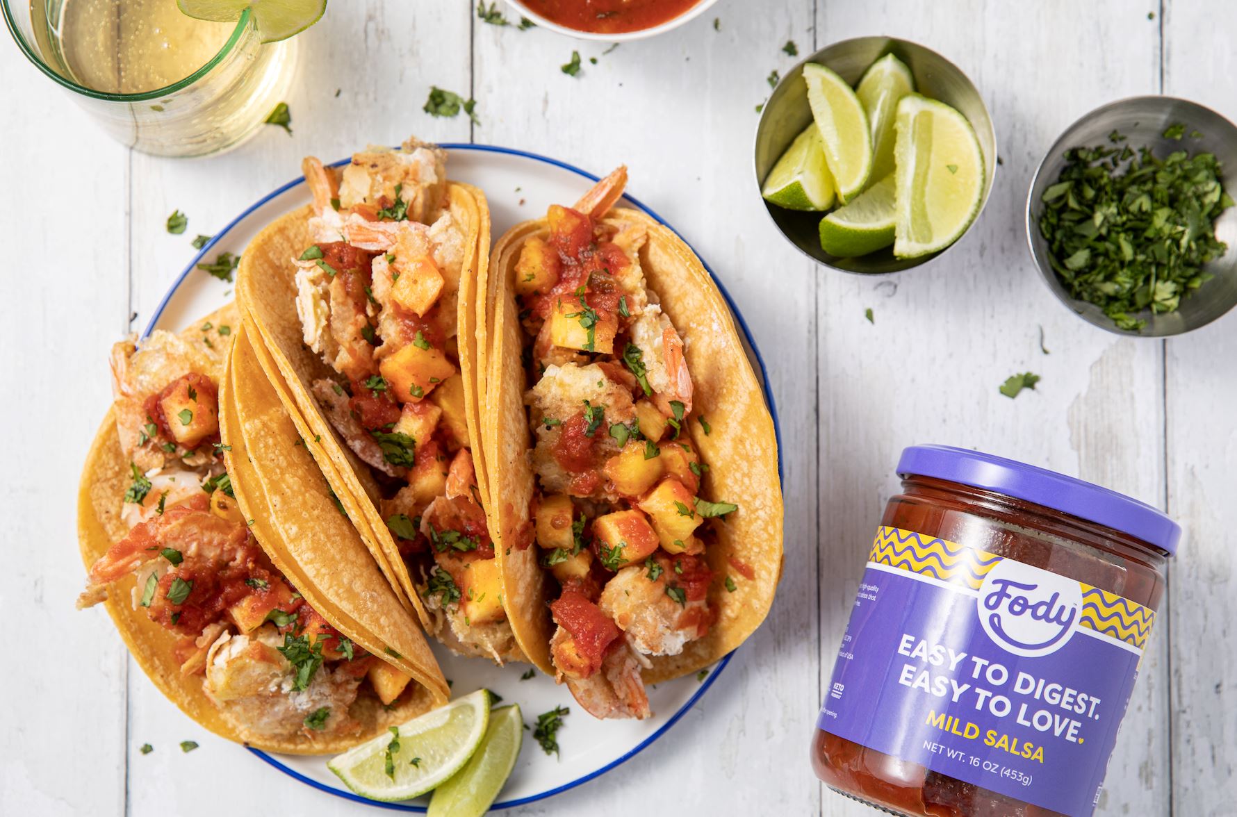 An image of Fody's Pineapple Coconut Shrimp Tacos on a Table beside a jar or Fody's salsa 