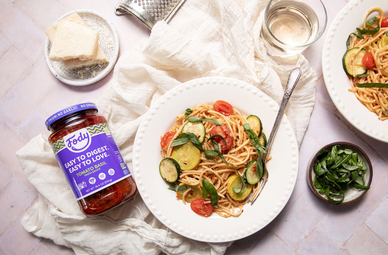 An image of Fody’s Summer Garden Pasta on a white plate on a crisp white napkin, beside a jar of Fody’s tomato-basil sauce.