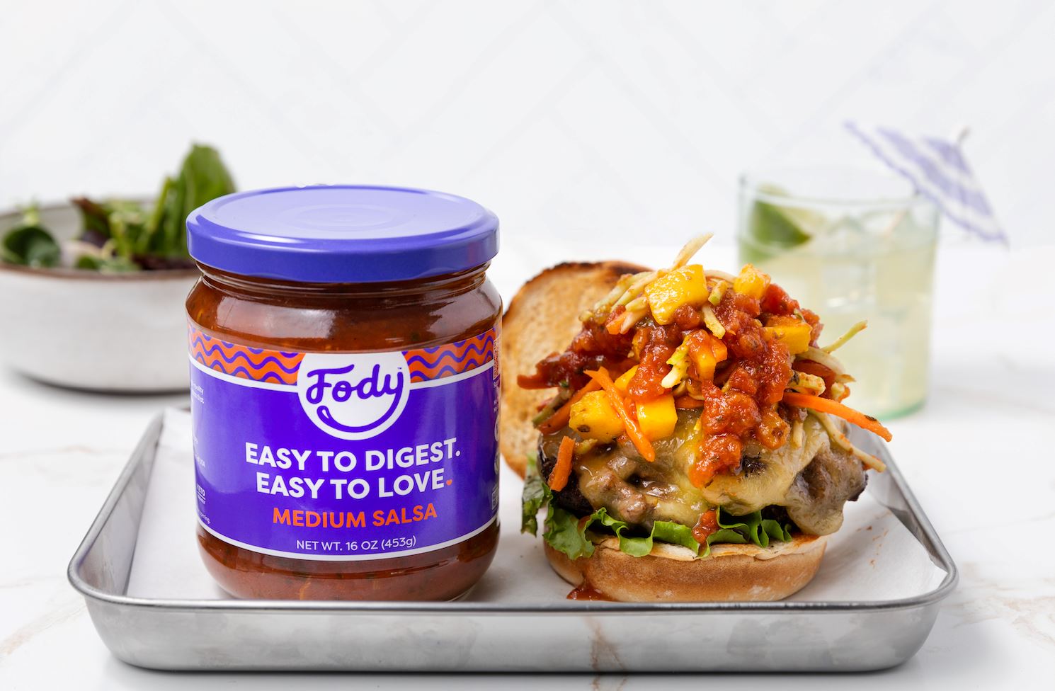 An image of Fody’s Jamaican jerk burger on a tin tray next to a jar of Fody’s medium salsa.