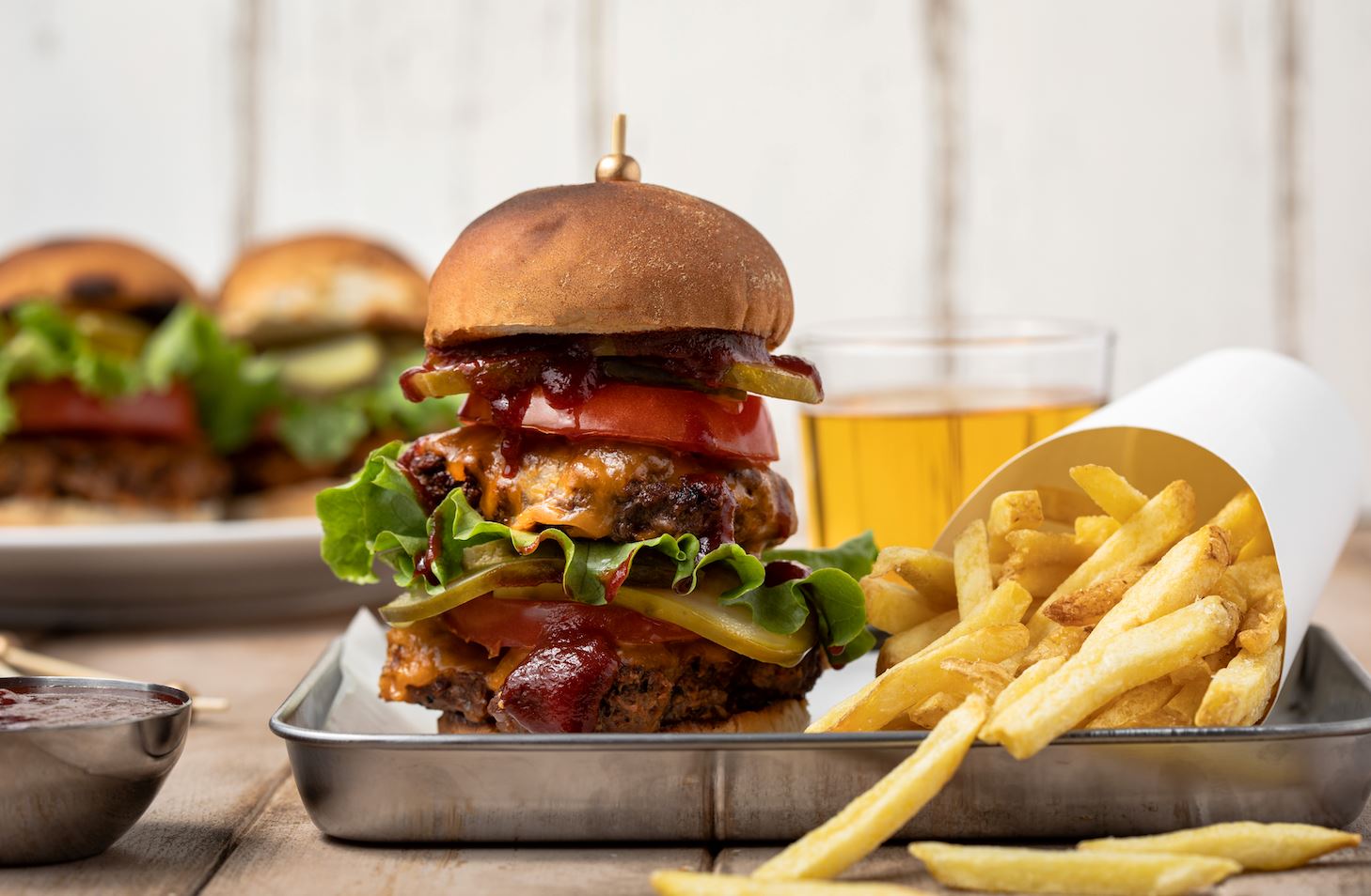 An image of Fody’s BBQ Homemade Smash burger on a tin tray beside a paper cup of fries spilling out onto the tray.