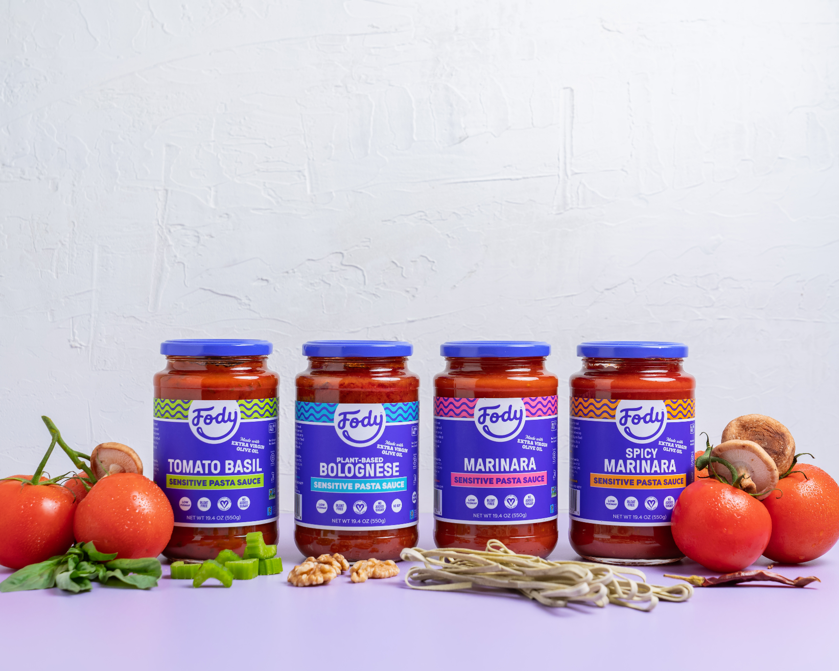 Four jars of Fody Low FODMAP pasta sauce displayed with noodles and fresh ingredients, showing IBS-friendly pasta sauce options made without onion or garlic.