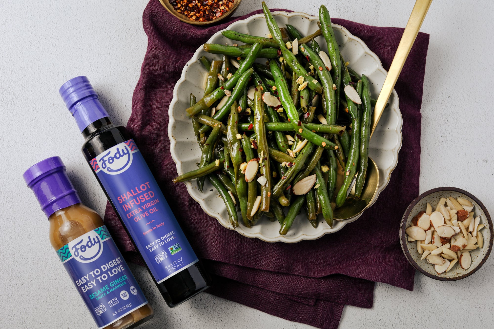 An image of a vegetable side dish of sesame ginger green beans served in a white bowl over a maroon trivet on a white background