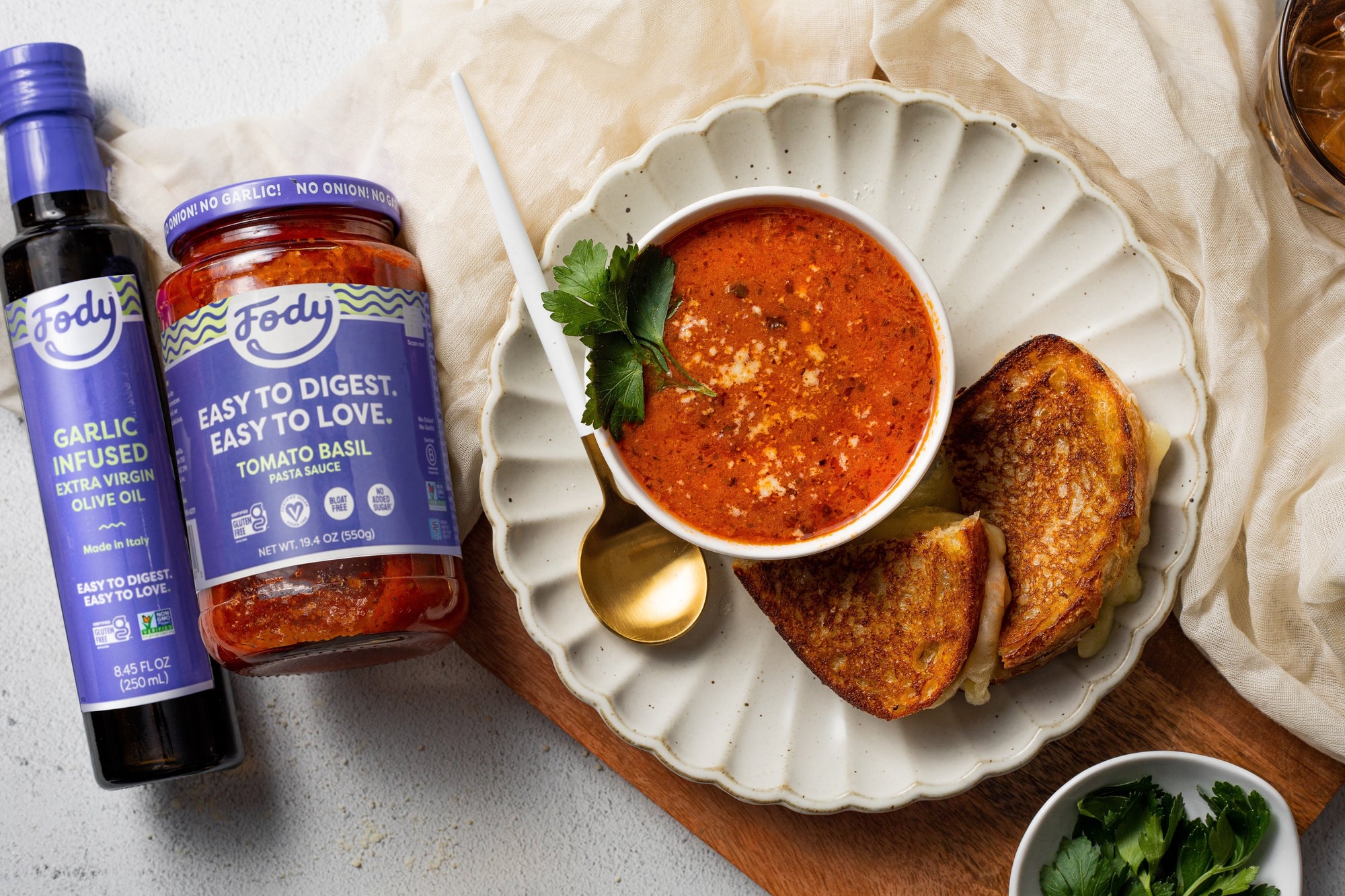A bowl of Fody's easy tomato soup on a plate with scalloped edges, beside a garlicky grilled cheese