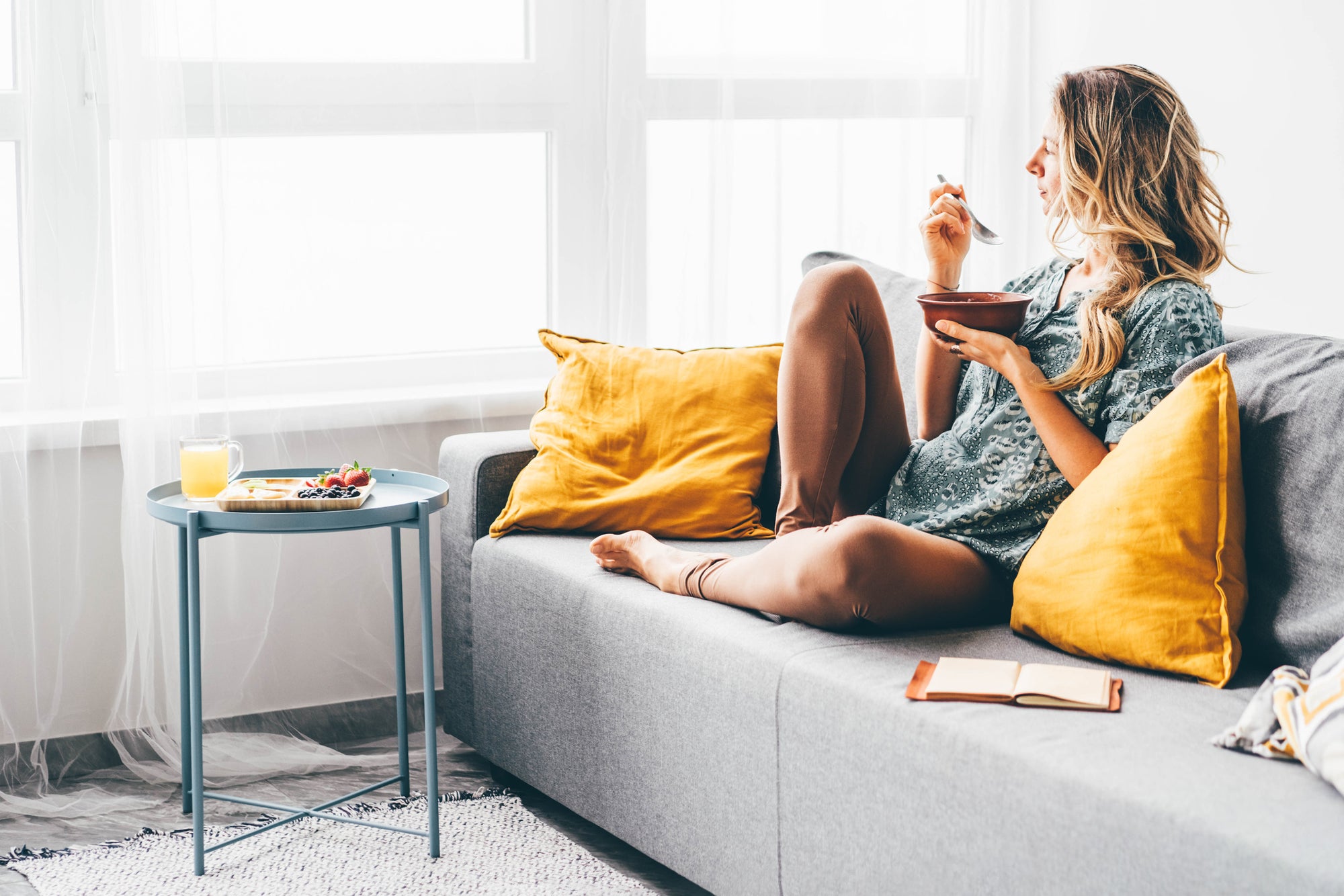 A woman sitting on a couch, looking relaxed as she eats a meal.