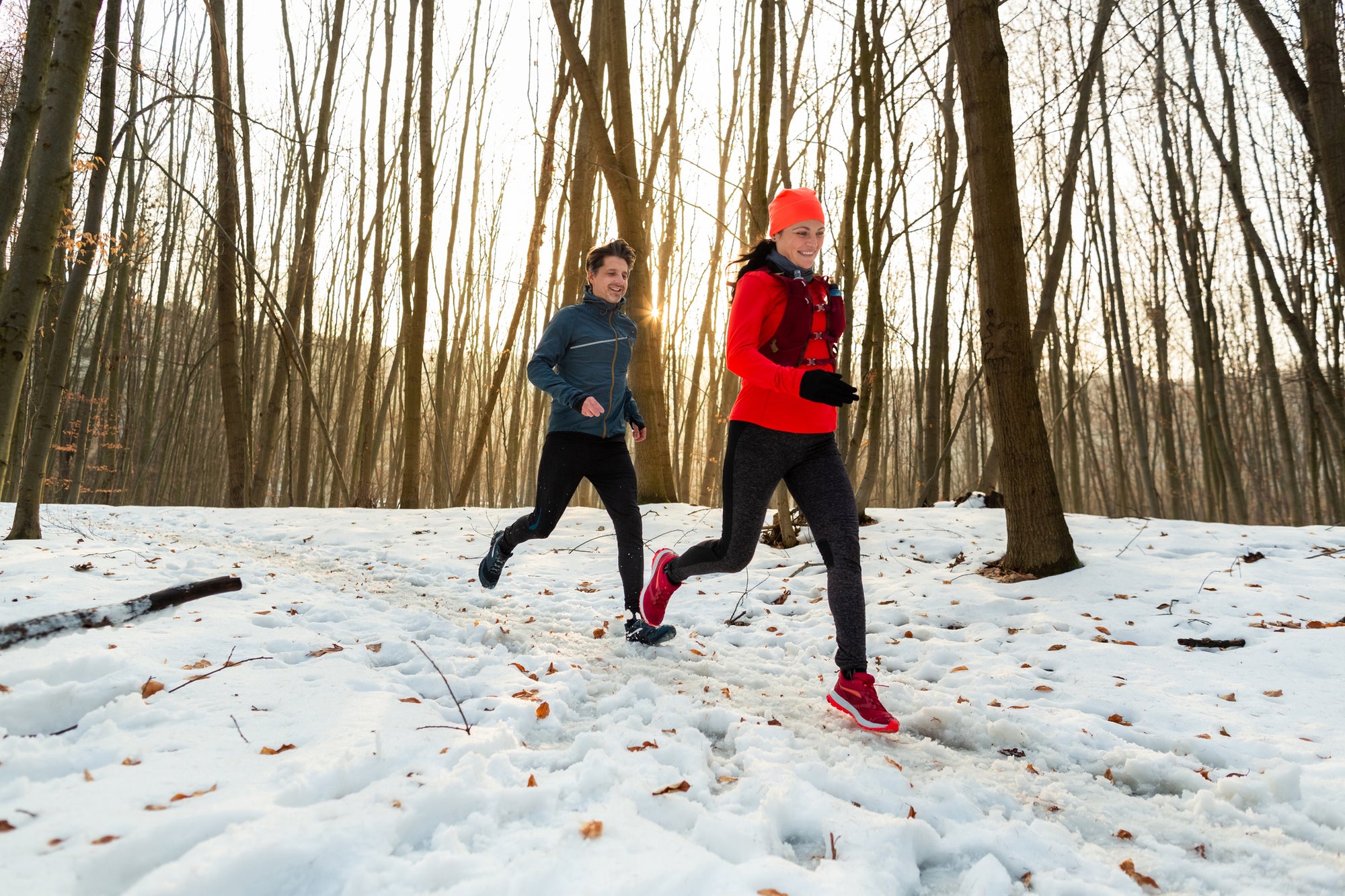 An image of a man and a woman beating the winter blues by going for a run in a snowy, woody path in early morning light.