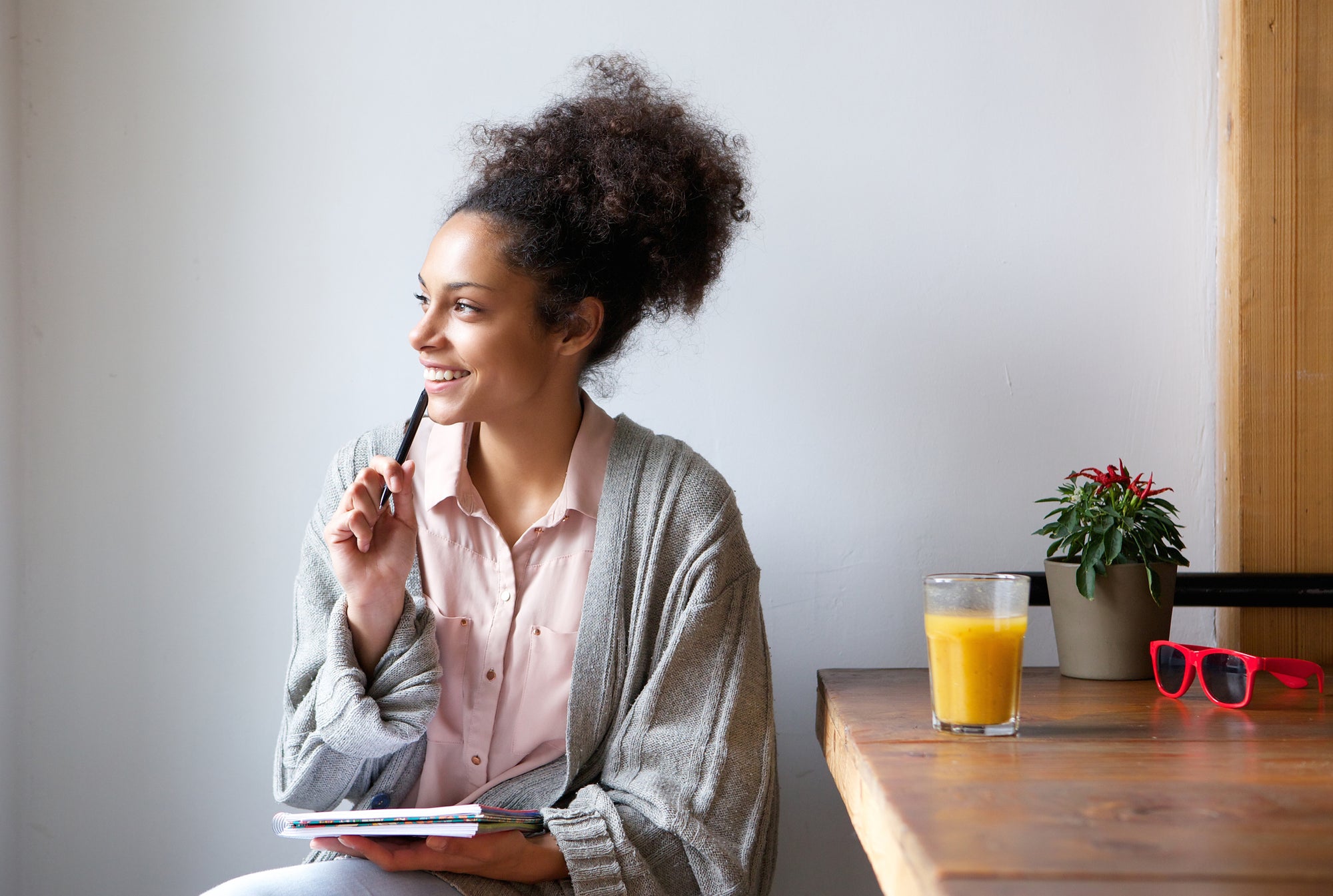 A young woman sitting in her home, smiling while holding a journal.