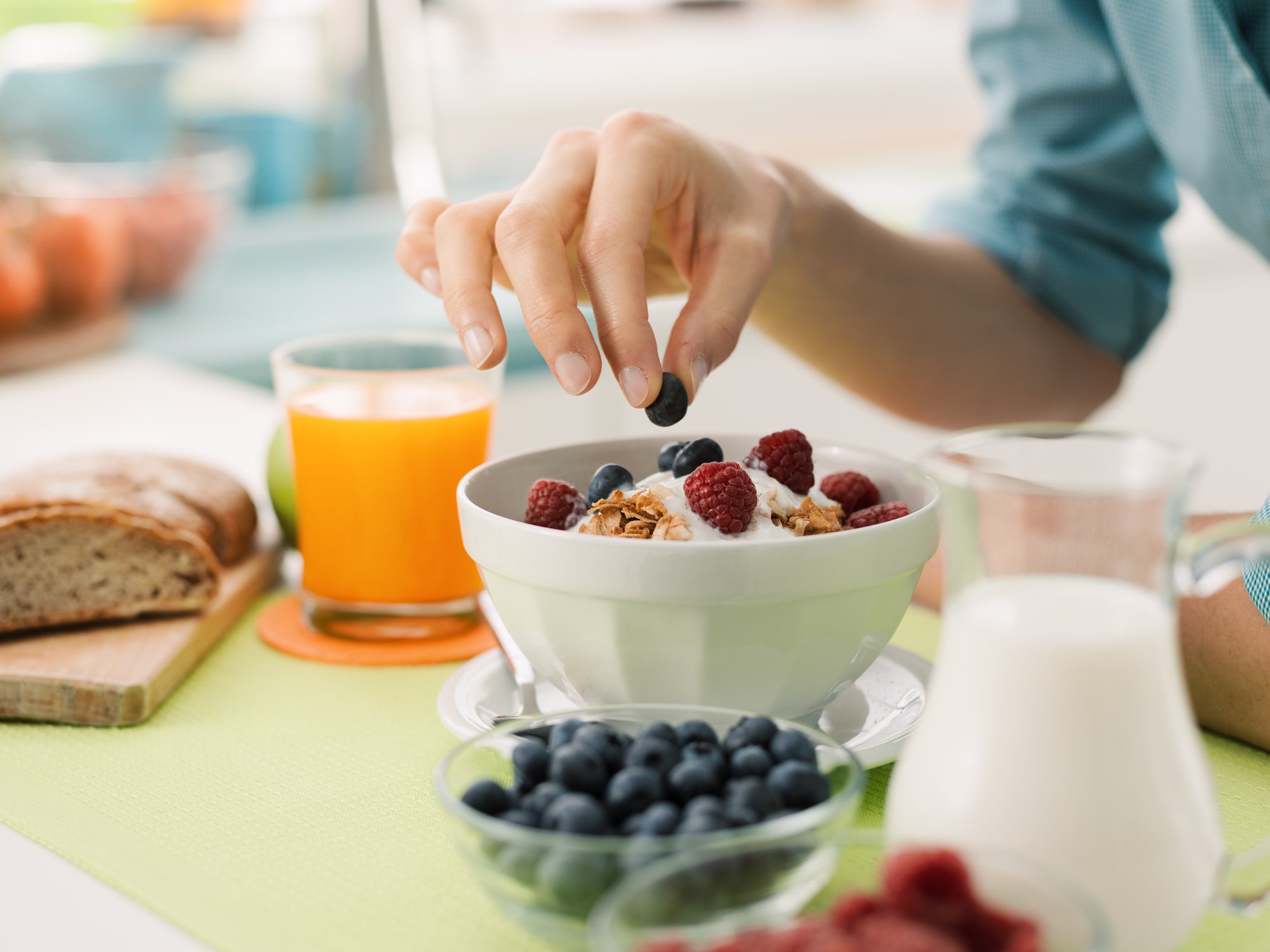 A woman’s hand plucking a blueberry from a healthy pre-workout snack of yogurt, oats and berries. 
