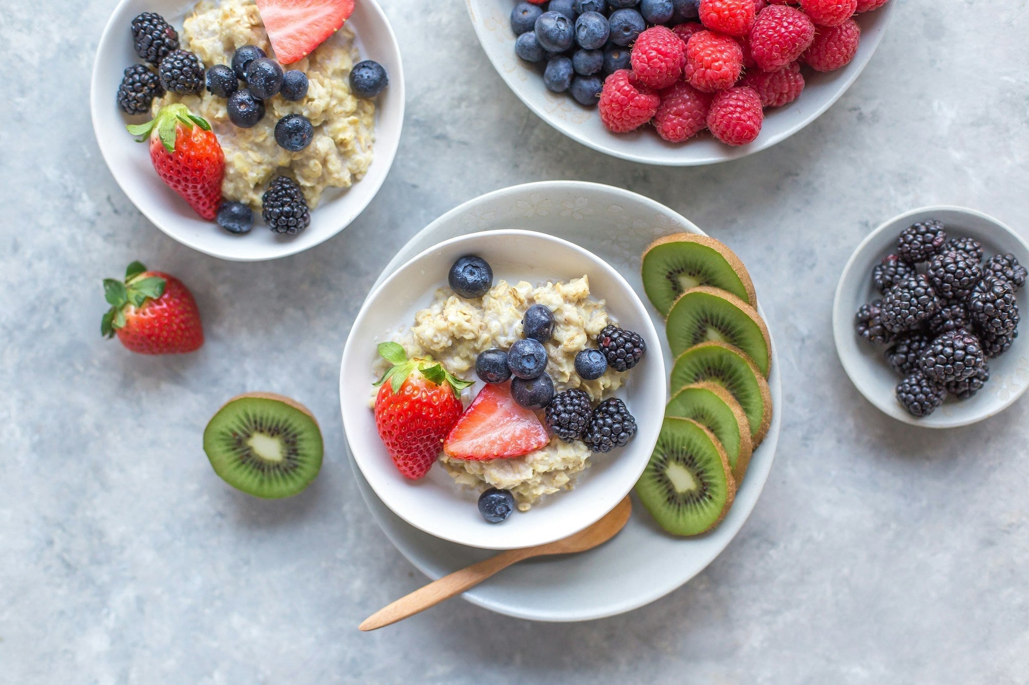 Overhead flat-lay of a bowl of oatmeal topped with fresh strawberries, blueberries, kiwi slices, and raspberries on a white surface, representing a Low FODMAP breakfast on an IBS diet plan.