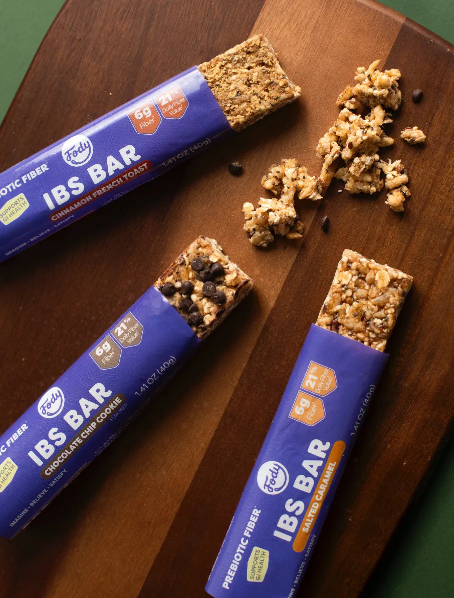 Hands slip a Fody Dark Chocolate Nuts and Sea Salt Snack Bar into a black backpack outdoors, a chocolate-coated nut bar ready for the day