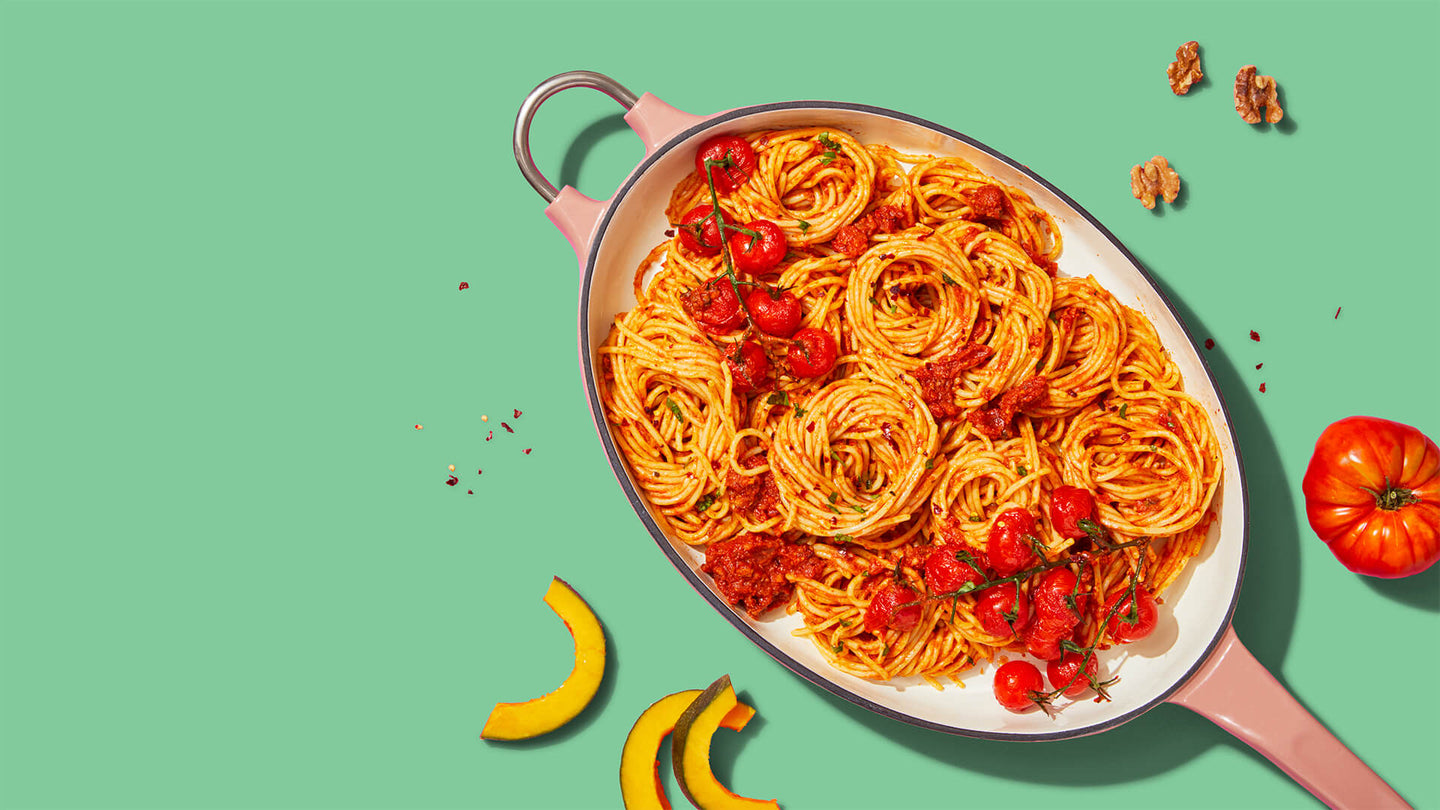 Spaghetti with tomato sauce and roasted cherry tomatoes in a pink pan on a green background.